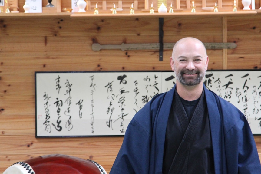 Head teacher of Bujinkan Tasmania Budo Dojo Duncan Stewart smiles broadly in front of the large shrine at the centre of his dojo