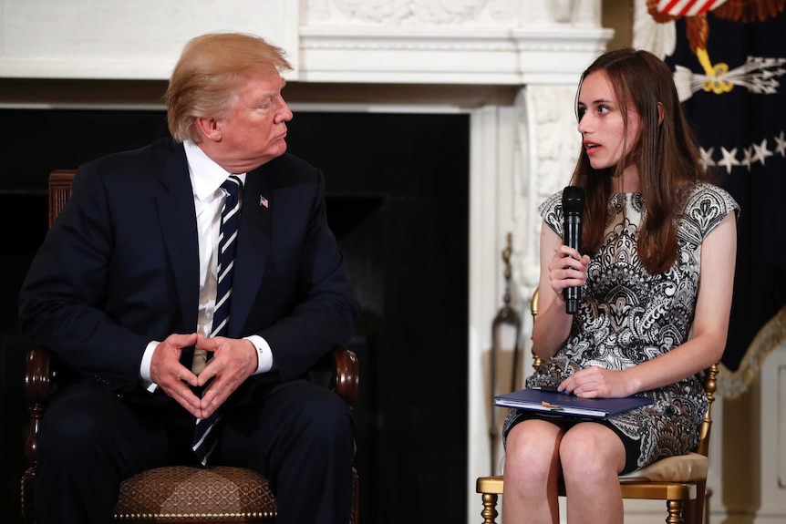 Donald Trump listens as a student sits next to him speaking.