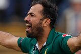 Wahab Riaz holds his arms outstretched with his mouth open as Aaron Finch turns his back to the bowler