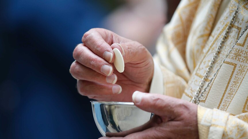 A close up of priest's hands holding a communion wafer.