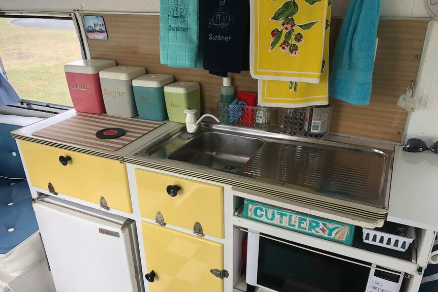 Photo of the kitchen sick with 60 anniversary towels, yellow drawers, pastel coloured containers, cutlery written on the draw