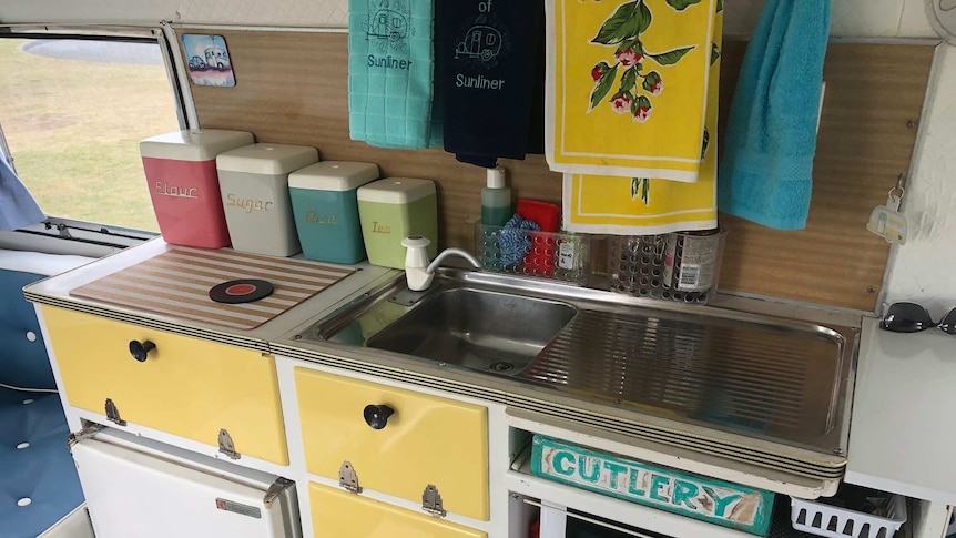 Photo of the kitchen sick with 60 anniversary towels, yellow drawers, pastel coloured containers, cutlery written on the draw