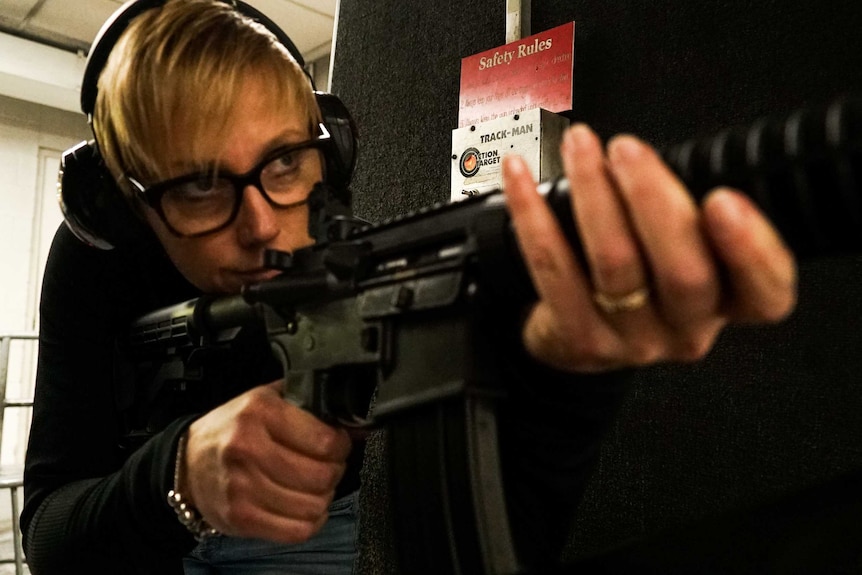 A close-up of a woman holding a weapon at a gun range
