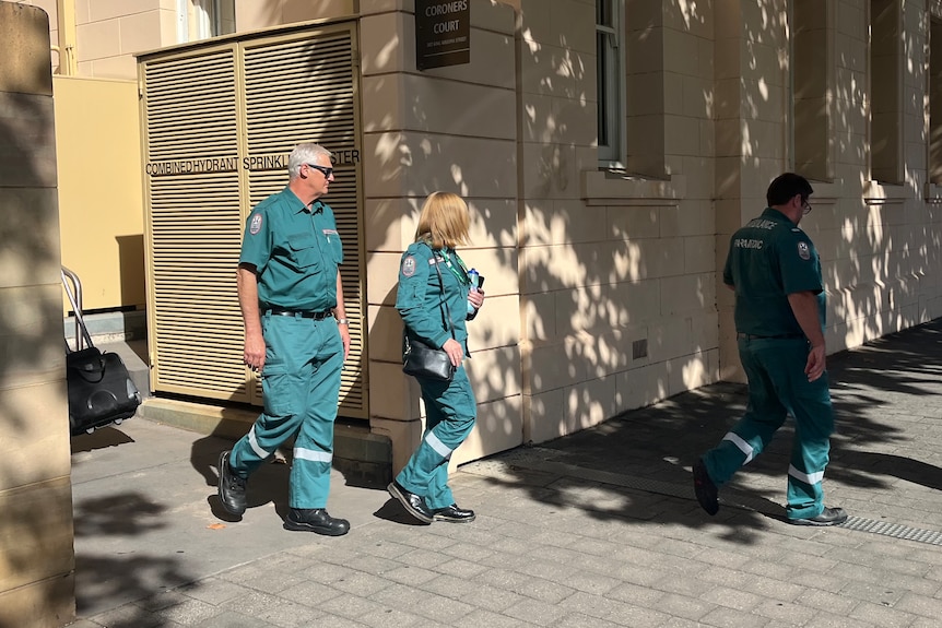 Paramedics in green work clothes walk out of Adelaide court building.