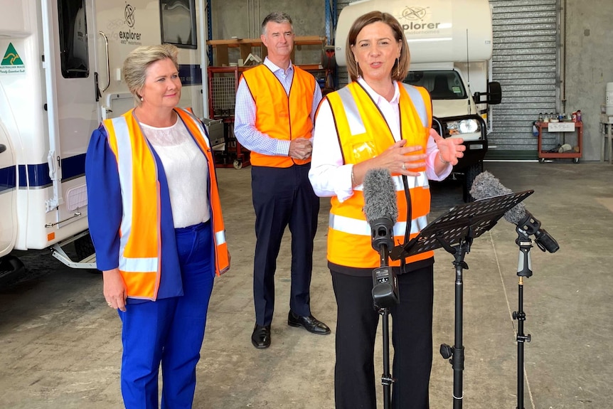 Woman in high-vis vest speaks to the media in a garage with campervans.