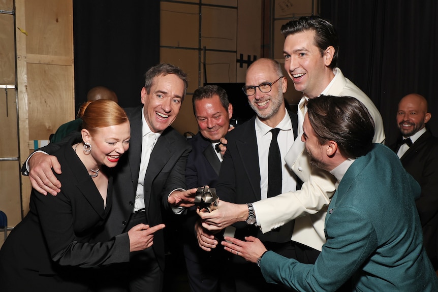 The cast all smile and hug as they gather in together and pose with their trophy.