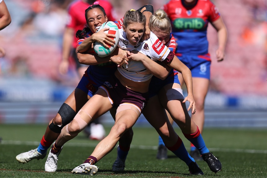 A Brisbane Broncos NRLW player is tackled by the Newcastle Knights.