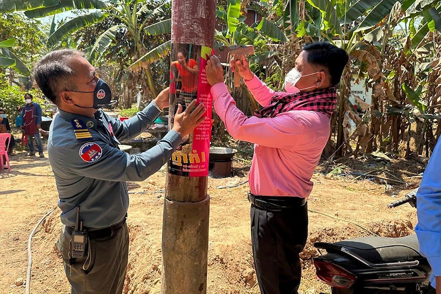 Two masked men put up a bird flu warning poster on a pole.