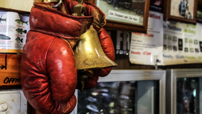 A pair of old red leather boxing gloves and a brass bell over the bar, with photos in the background.