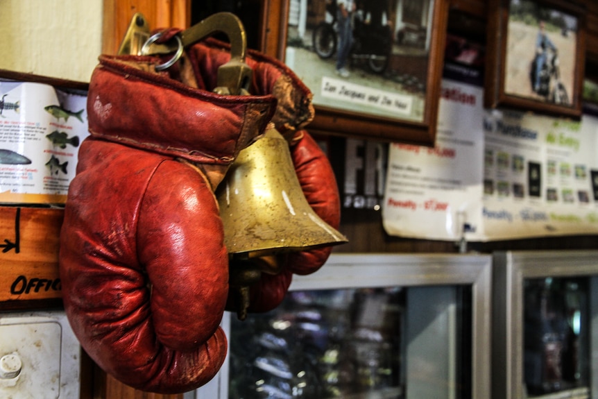 A pair of old red leather boxing gloves and a brass bell over the bar, with photos in the background.
