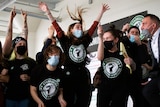 A group of people wearing uniforms and masks jump in the air. 