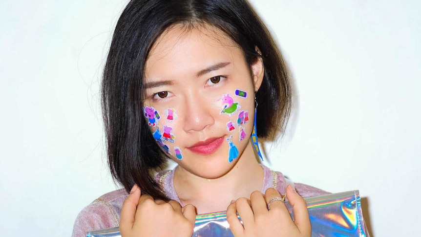 A woman has stickers on her face and holds a metallic bag.