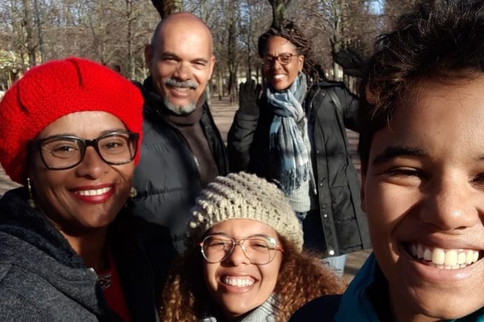 A woman wearing glasses and a red beanie stands next to two children a man and another woman