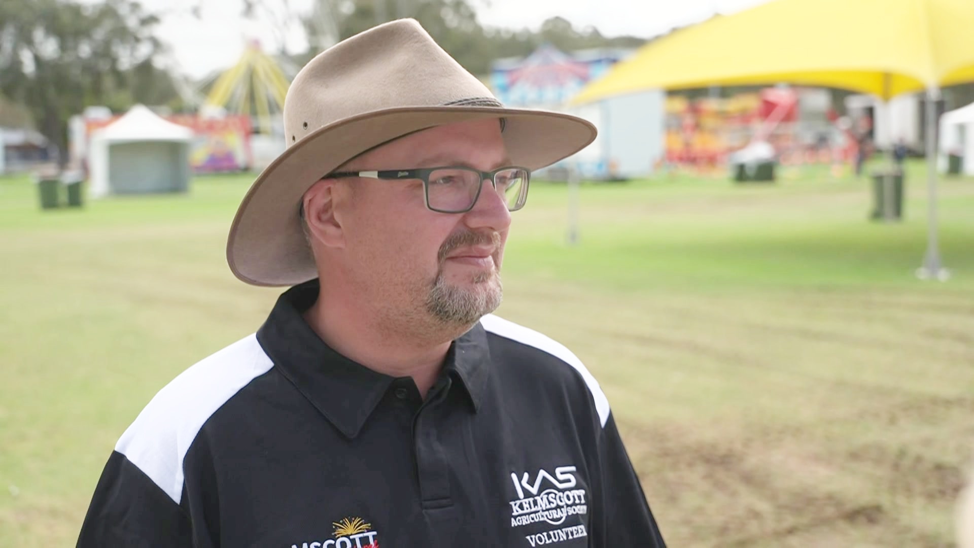 Daryl Dawes wears a wide-brimmed hat and a polo shirt while talking to reporters in a park. 