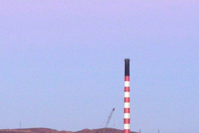 A red and white candy-striped smoke stack rises above the industrial grounds of a smelter work site.