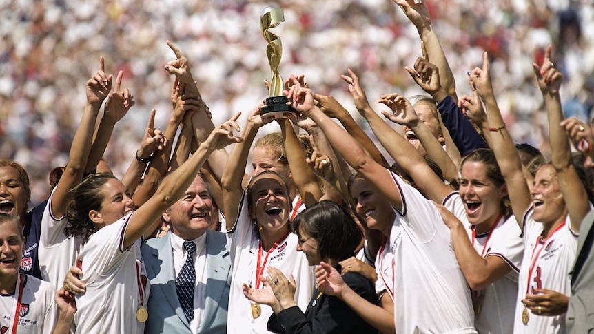 Women soccer players wearing white lift a trophy