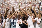 Women soccer players wearing white lift a trophy