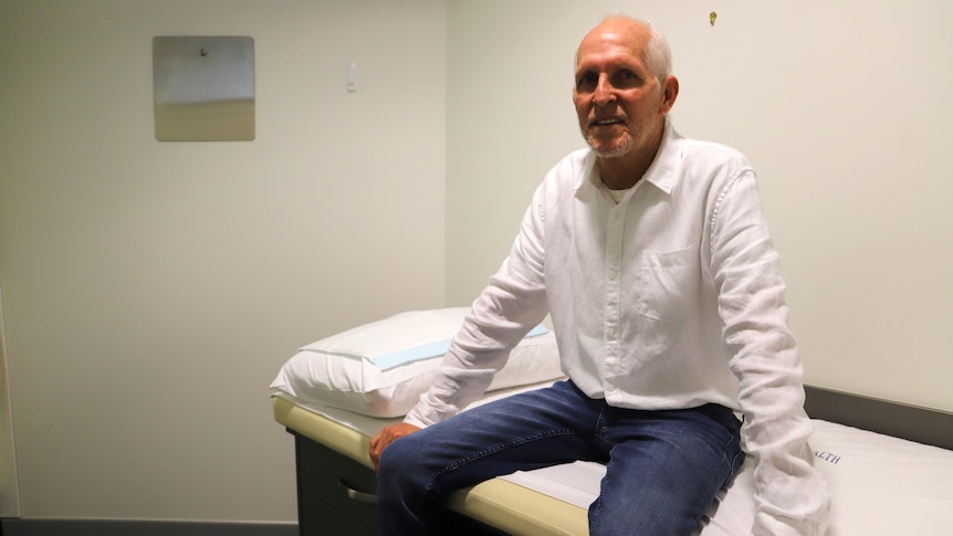 man in white shirt with white hair sits on hospital bed