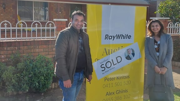 a man and a woman smiling infront of a SOLD sign on a house