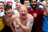 A number of England fans, some of them shirtless, celebrate in the direction of the camera