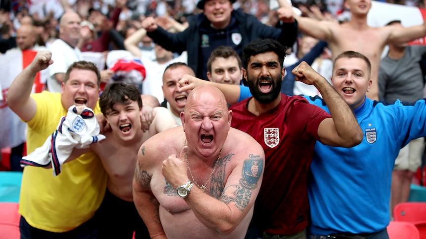 A number of England fans, some of them shirtless, celebrate in the direction of the camera