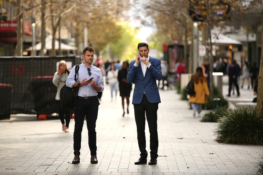 A wide shot of Basil Zempilas in a suit on the phone in the middle of a busy Murray Street Mall on a spring day.