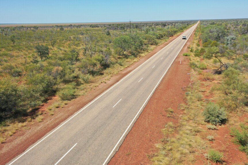 A ute drives along a lonely highway in the outback