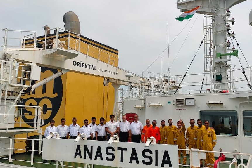 Crew stand on the deck of the bulk carrier Anastasia. It is a large ship and they seem very small by comparison.