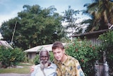 Joshua, and Australian man in ADF uniform, sits arm in arm with a Papua New Guinean man in a garden.
