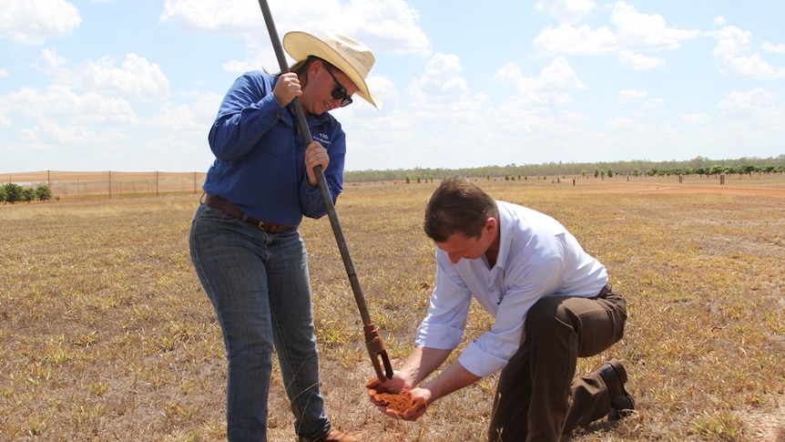 Teagan Alexander pours soil into the hands of Willem Westra van Holthe while standing in a bare paddock