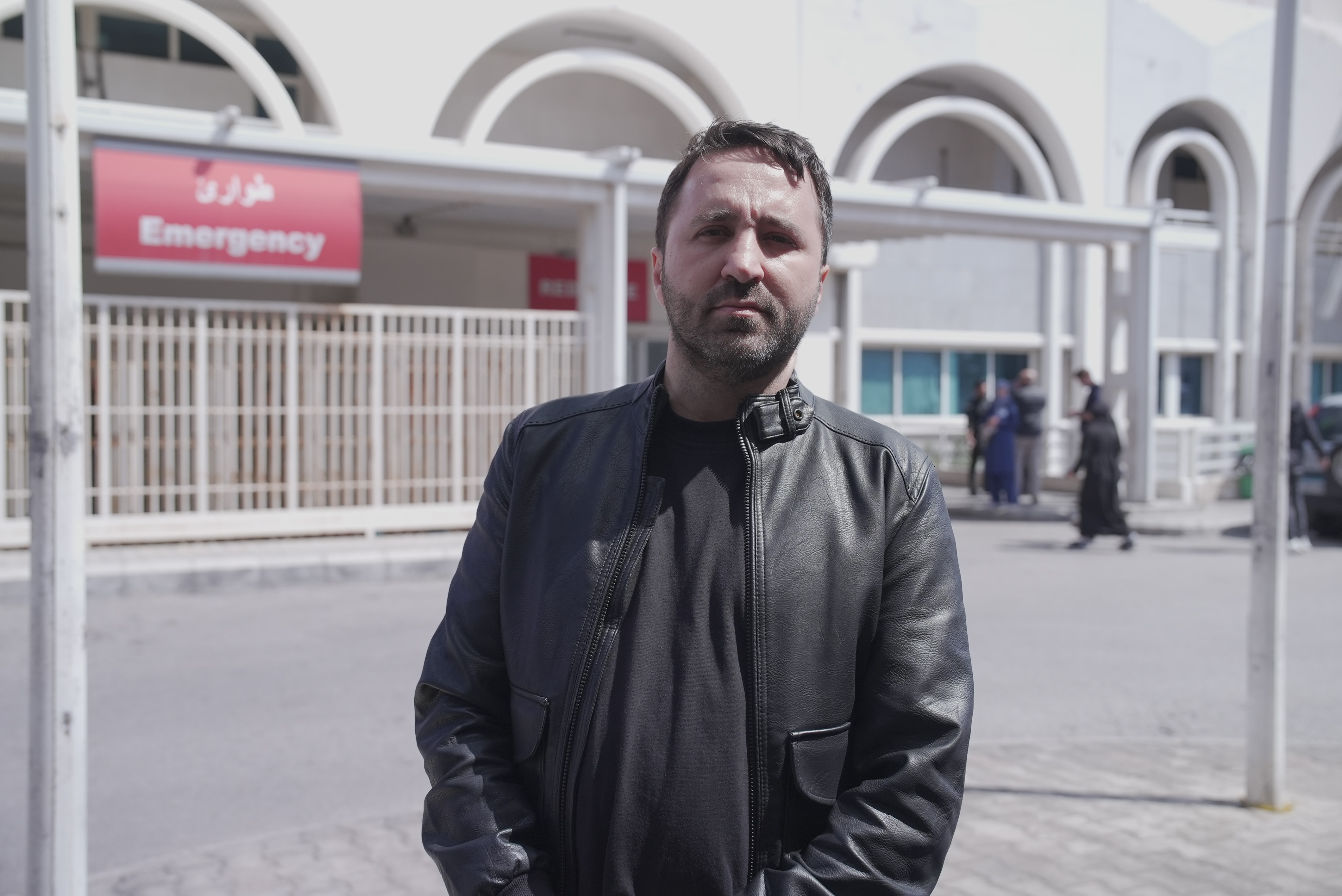 A man in a leather jacket stands out the front of an emergency ward.