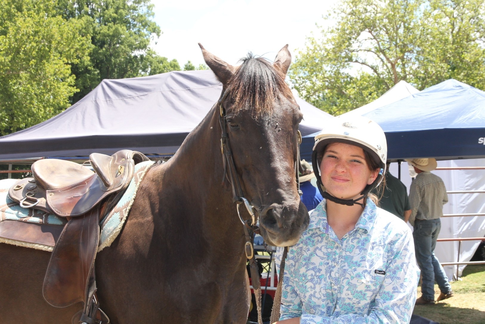 Uma adolescente vestindo uma camisa estilo ocidental e um capacete de equitação, além de meia-calça marrom.