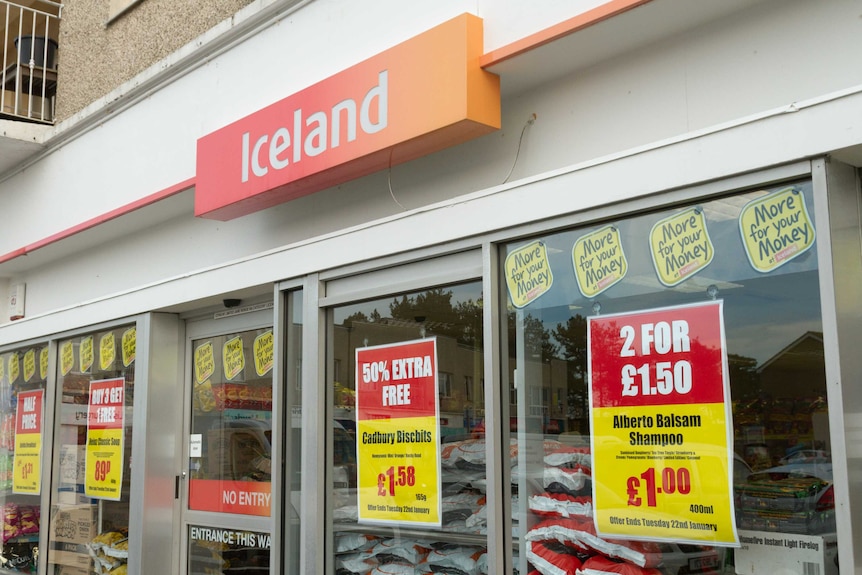 A white storefront with an orange sign saying Iceland. There are promotions on the window.