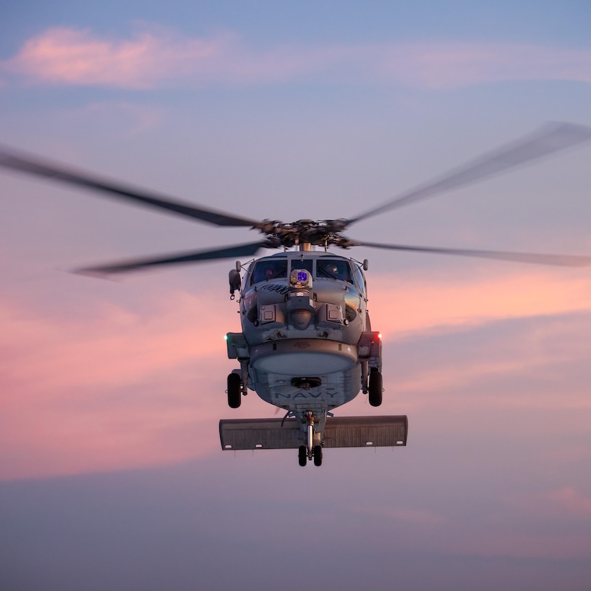 A helicopter flying in the air at sunset.