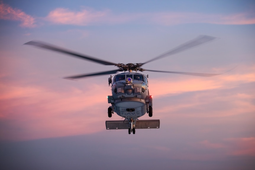 A helicopter flying in the air at sunset.