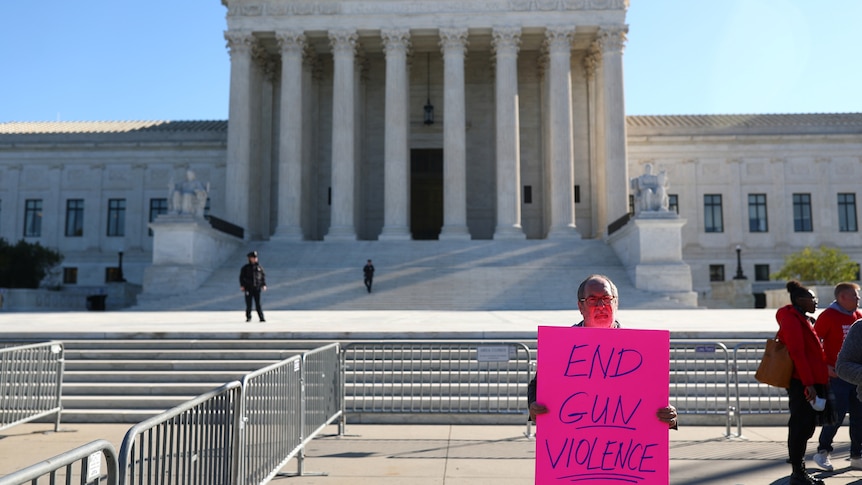Man stands outside the Supreme Court building with an 'End Gun Violence' sign.