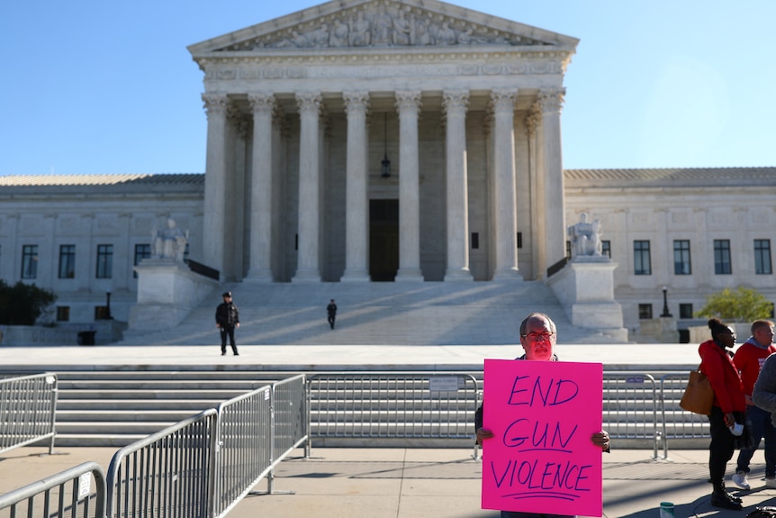 Man stands outside the Supreme Court building with an 'End Gun Violence' sign.