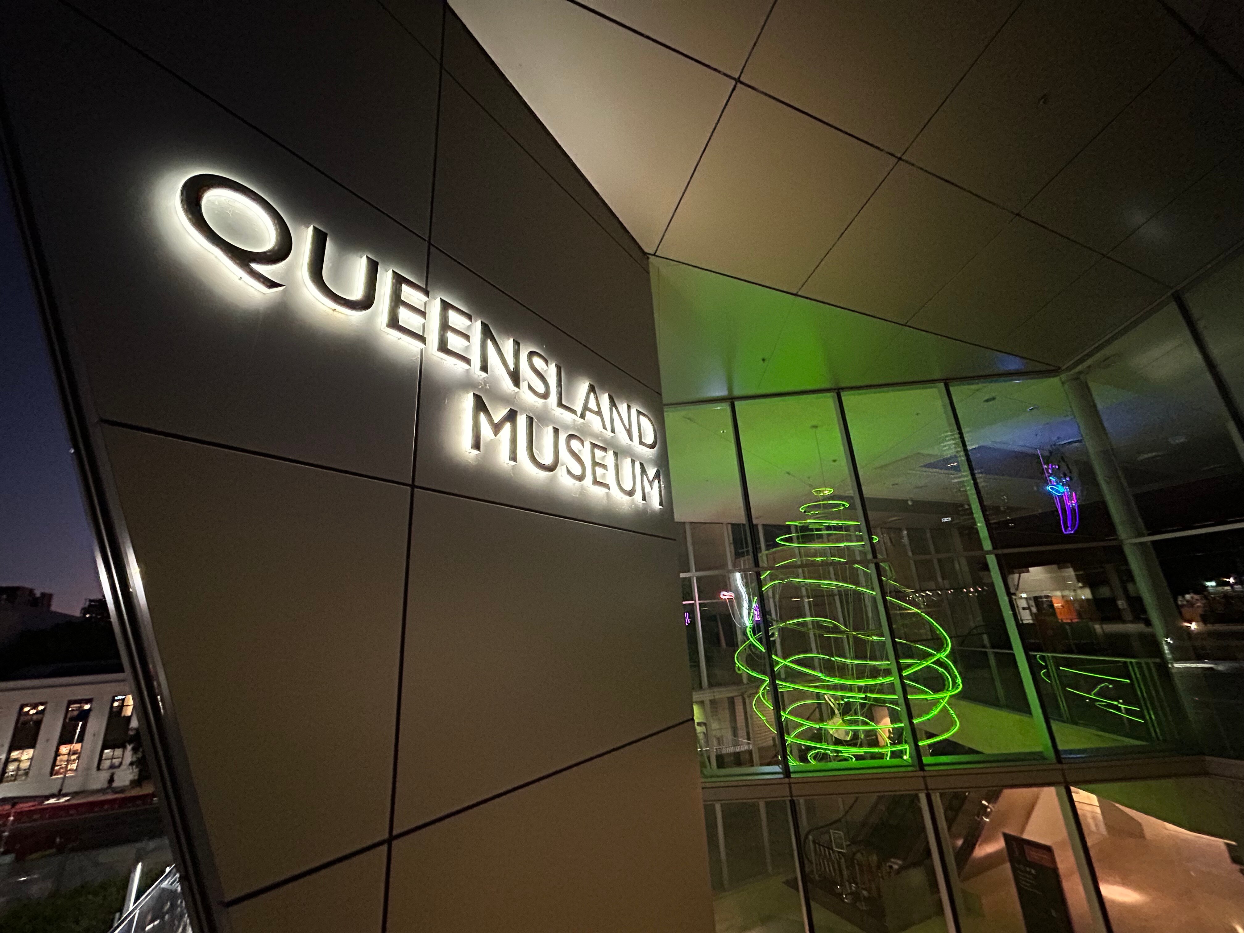 A sign in lights that says 'QUEENSLAND MUSEUM' situated next to a window.