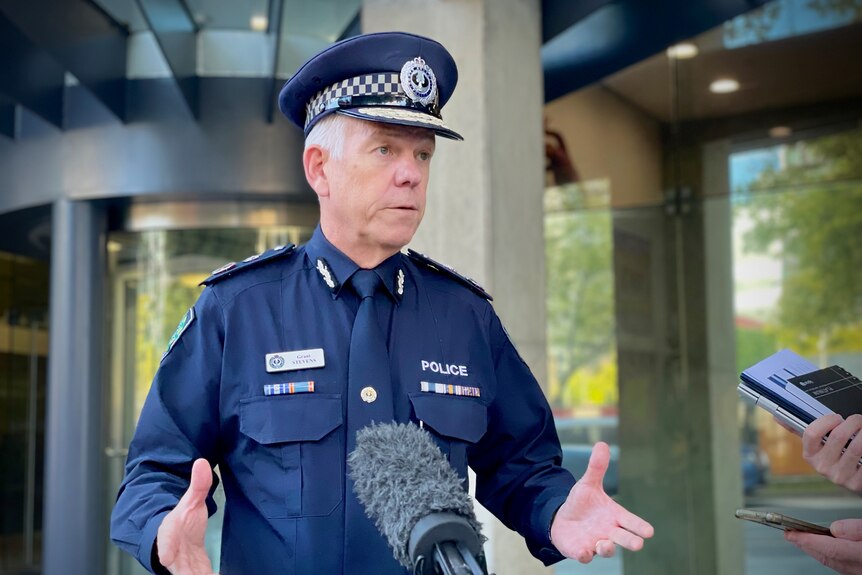 Un homme vêtu d'un uniforme de police bleu foncé parle à des microphones à l'extérieur d'une porte tournante