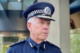 A man wearing a dark blue police uniform speaks to microphones outside a revolving door