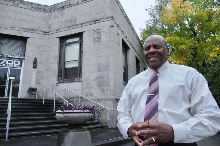 A man in a tie smiles outside a building.