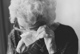 A black and white photo of an elderly woman wiping her eyes with a tissue.