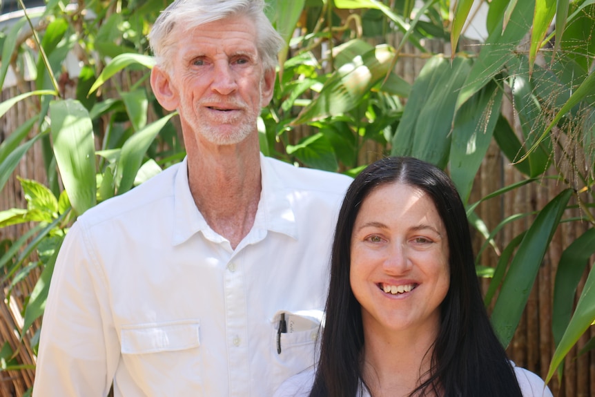 Young woman, long black hair, older man, grey hair and beard, both smile, stand in a garden.