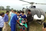 group of men push a stretcher carrying a child, with helicopter in background