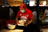 An employee wearing a face mask to protect against the coronavirus clears a table at a restaurant.