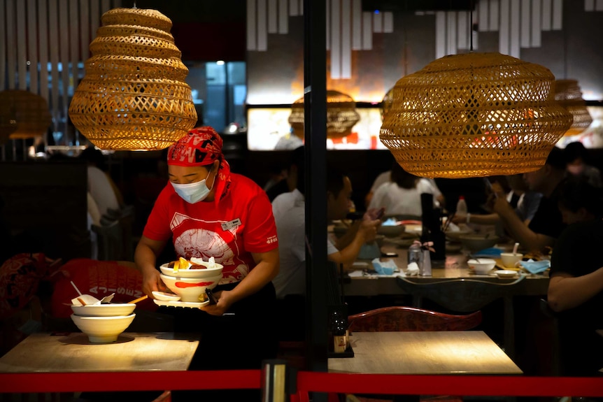 An employee wearing a face mask to protect against the coronavirus clears a table at a restaurant.