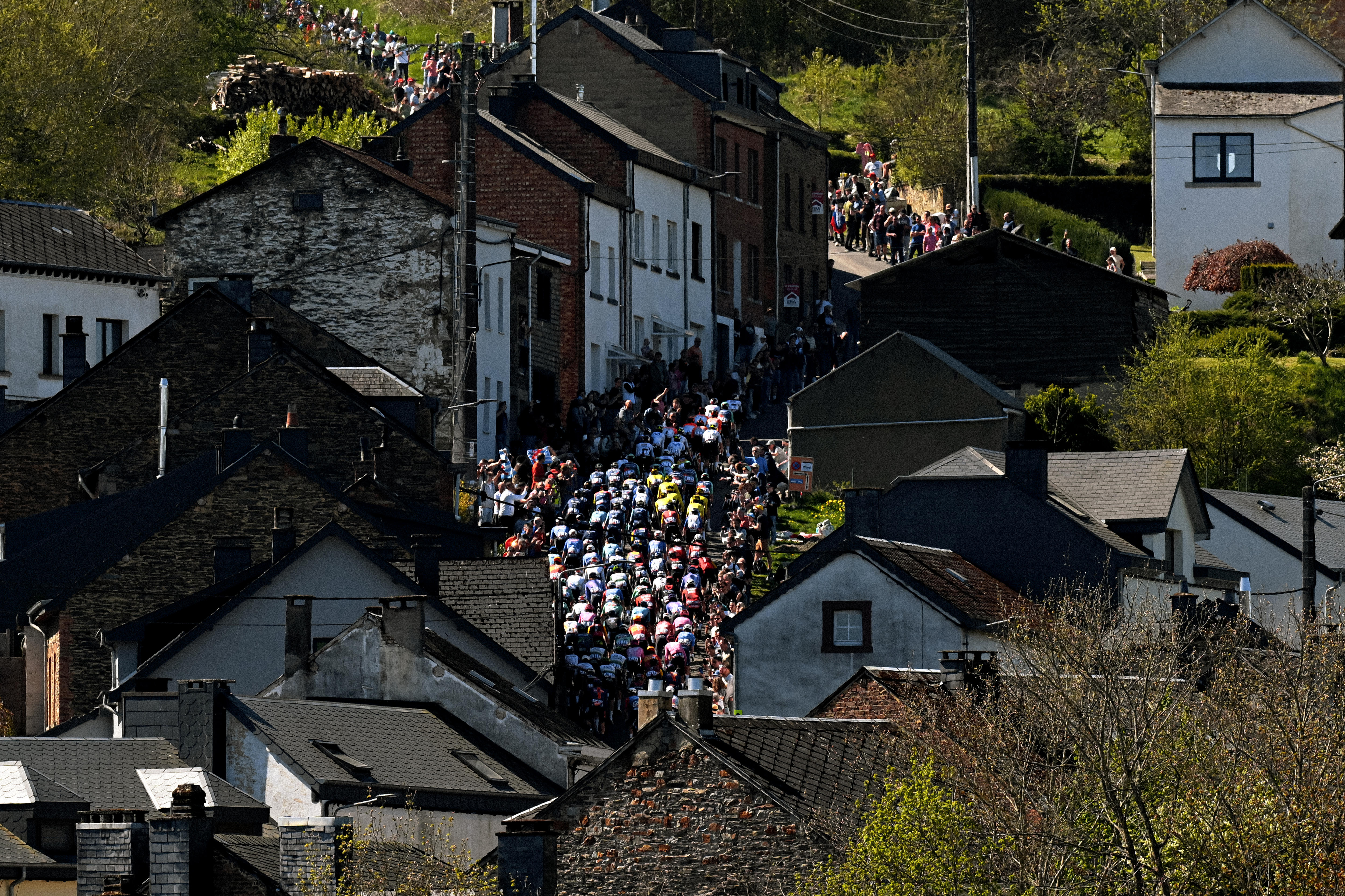 Uma foto aérea mostrando ciclistas em uma estrada estreita entre casas antigas.