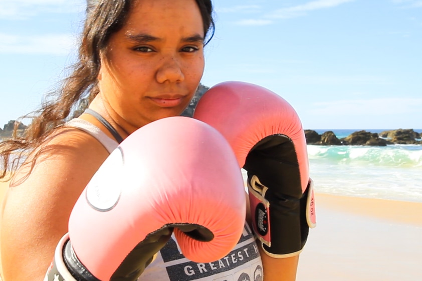 Portrait of young woman on beach wearing boxing gloves.