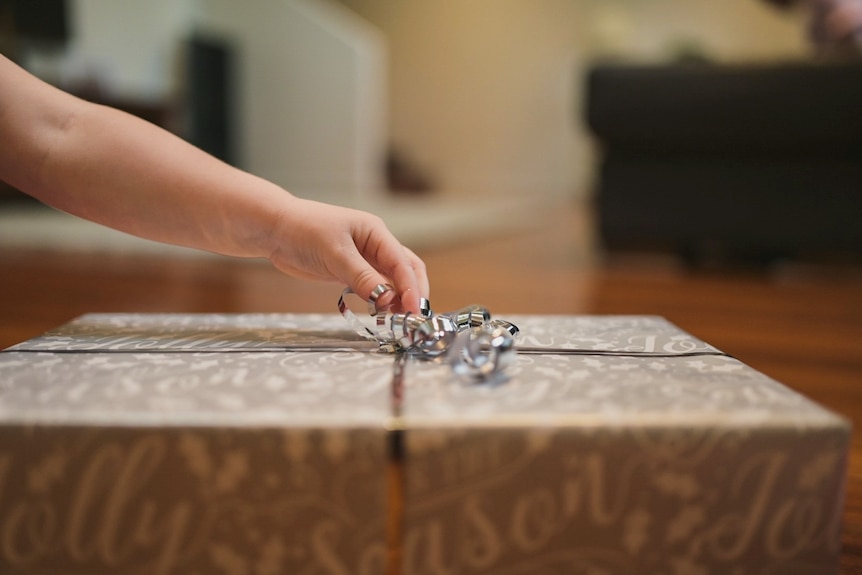 A child's hand opens a Christmas present.