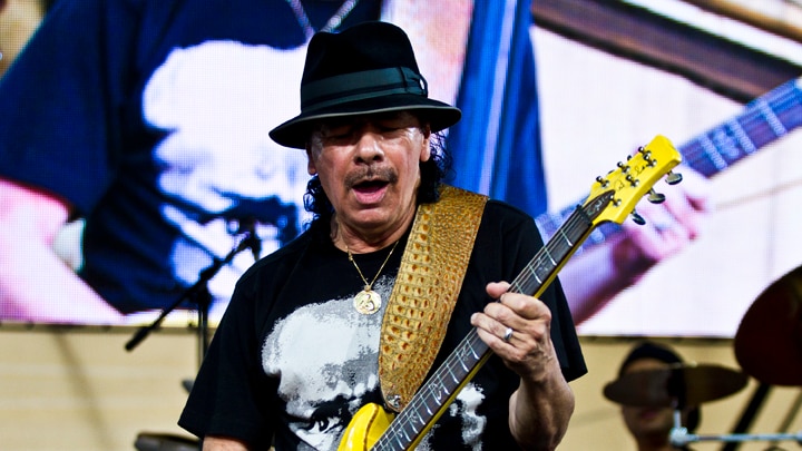 Carlos Santana on stage playing a bright yellow guitar